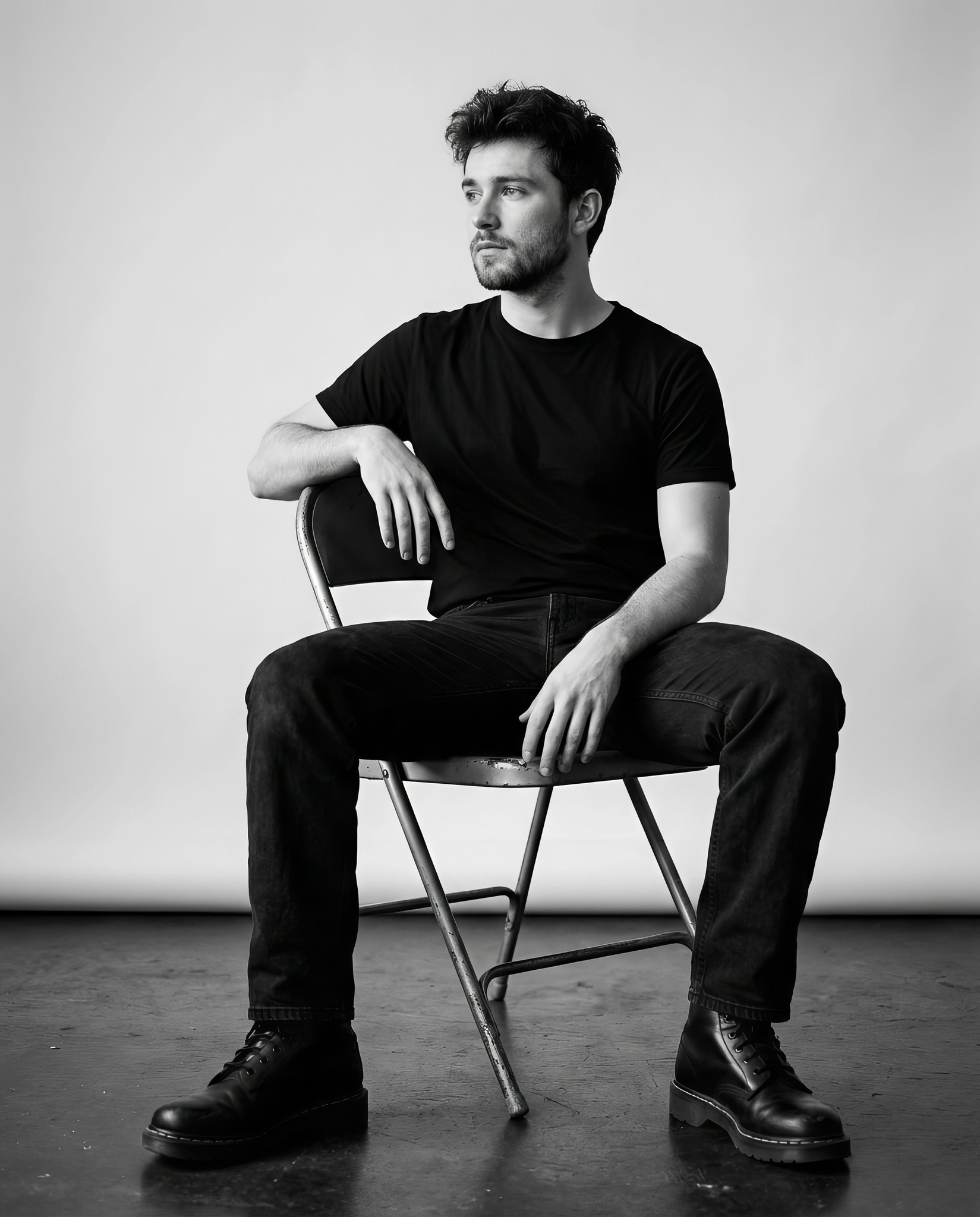 Ultra-realistic black and white portrait of a young man sitting on a simple metal folding chair in a
