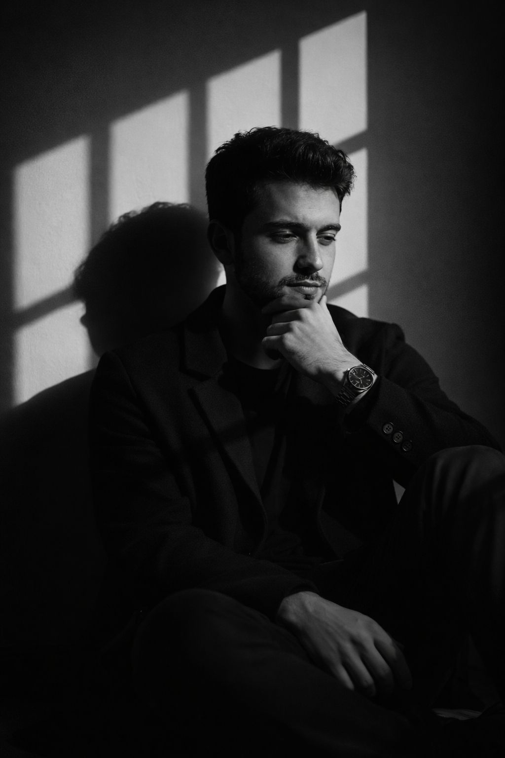 Ultra-realistic cinematic black and white portrait of a young man sitting on the floor beside a wall