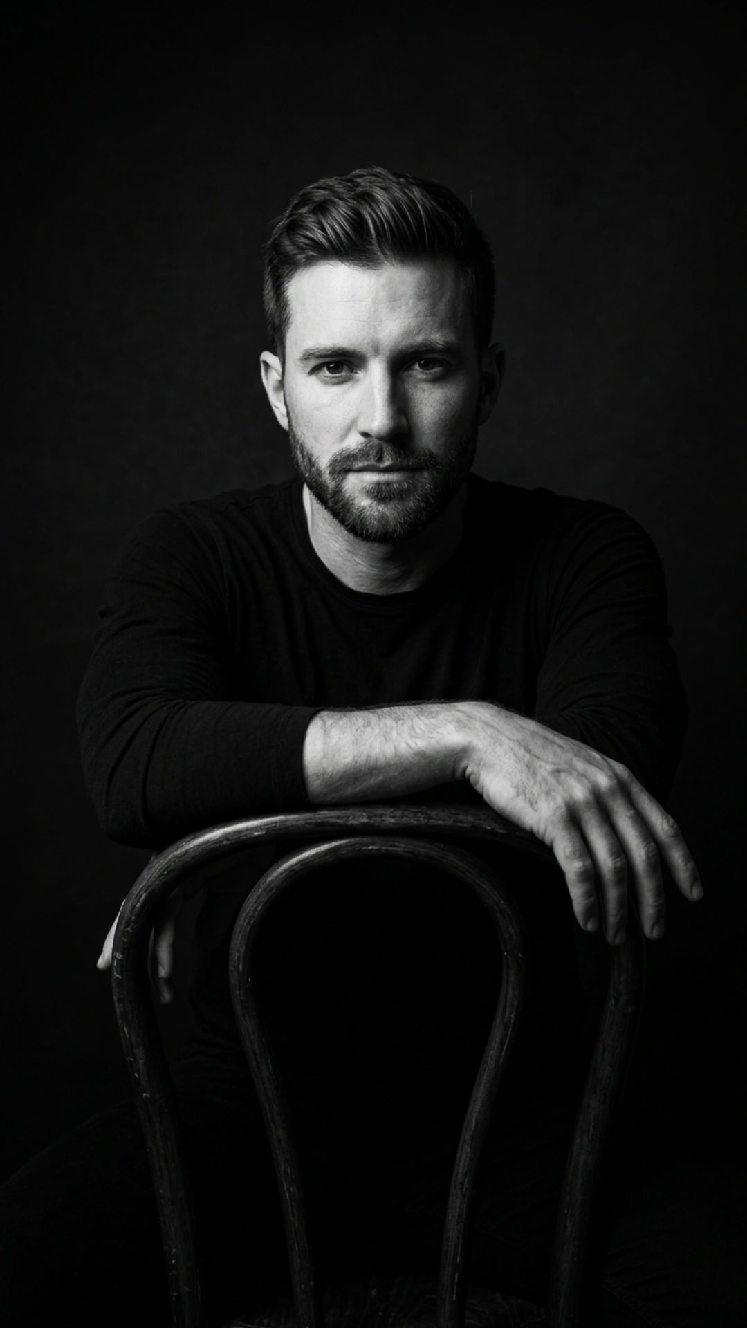 Ultra-realistic 8K cinematic black-and-white portrait of a man, STRICT pose: sitting behind a chair,