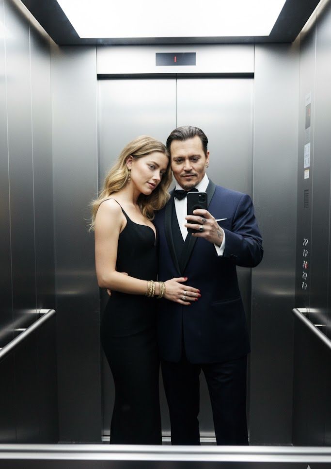 A couple takes a stylish selfie inside a modern stainless-steel elevator. The man ( use uploaded ima