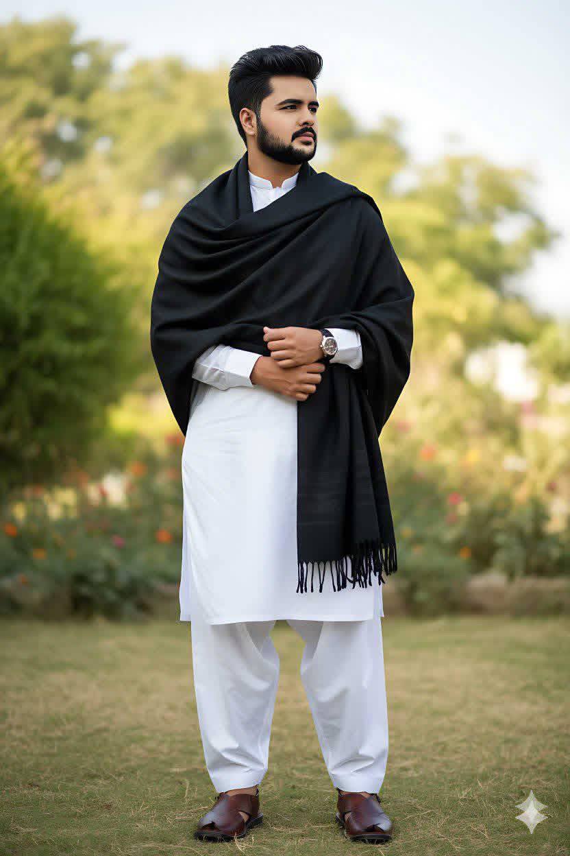 A young man wearing a white kameez shalwar with a black shawl draped over his shoulders. He is stand