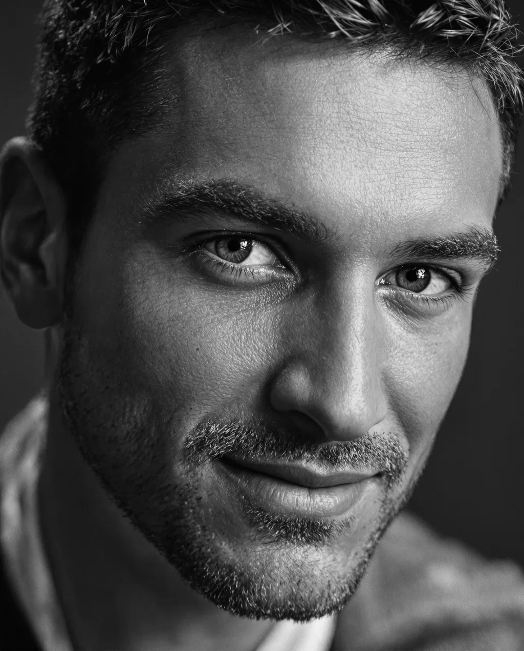 A close-up in black and white of a handsome man with chiseled features, perfectly trimmed hair and c