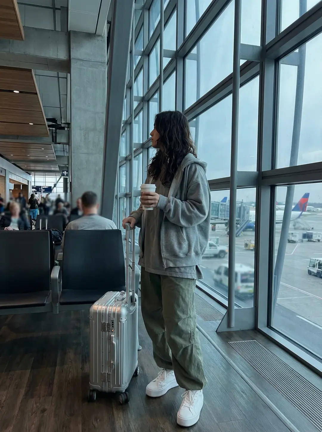 A young adult with long, naturally styled hair wears an oversized hoodie layered over a loose, casua
