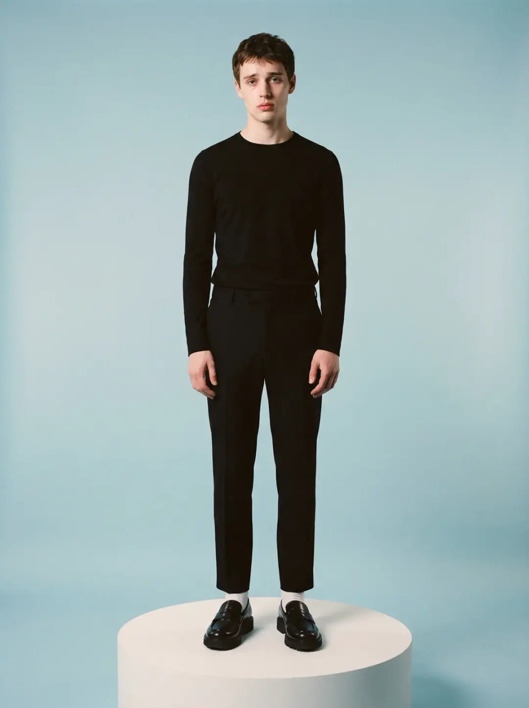 In a minimalist studio with a soft muted pastel blue backdrop, a Young adult Caucasian Male model wh